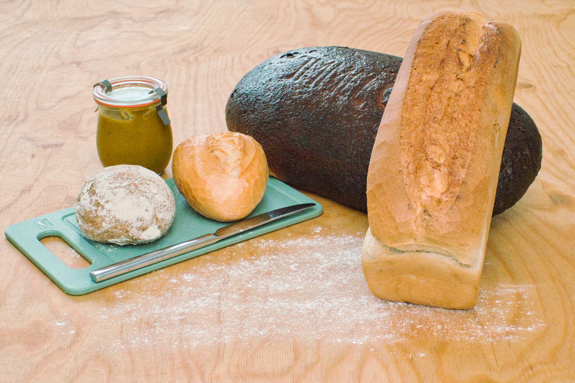 Brot mit Weissbrot, Brötchen dazu ein Brettchen mit Messer und Paste auf Leimholz Naturbelassen